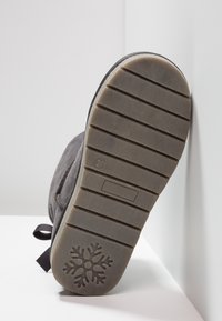 Šedá podrážka boty s vroubkovanou strukturou, ve středu se sněhovou vločkou. Mírně opotřebovaný vzhled s plochým, odolným designem.