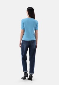 Helles blaues Kurzarmoberteil, kombiniert mit dunkelblauen, locker sitzenden Jeans und schwarzen High Heels. Das Outfit zeichnet sich durch ein schlichtes Design und eine simple Textur aus.