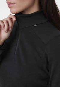 Sudadera de forro polar negra con un cuello alto, que cuenta con una cremallera half-zip y costuras en los hombros. Incluye un pequeño logo en el área del pecho izquierdo.