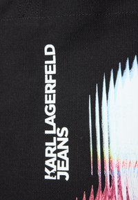 Czarna tkanina dżinsowa z białym napisem "KARL LAGERFELD JEANS" oraz gradientowym wzorem z niebieskimi, różowymi i pomarańczowymi akcentami na krawędzi.