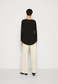 Black long-sleeve top with a rounded hem, paired with cream wide-leg trousers, and black heeled shoes. Smooth texture, simple design.
