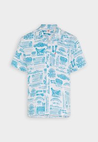 Camicetta a maniche corte in cotone bianco con etichette e loghi vintage stampati in blu. Presenta un colletto classico e chiusura con bottoni.