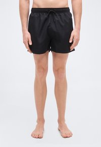 Μαύρα μαγιό σορτς με ελαστική μέση και κορδόνι, με λεία υφή και μήκος πάνω από το γόνατο. Χωρίς ορατά λογότυπα ή σχέδια.
