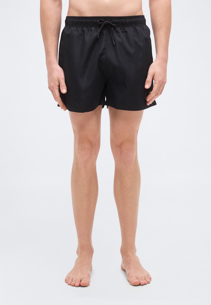 Μαύρα μαγιό σορτς με ελαστική μέση και κορδόνι, με λεία υφή και μήκος πάνω από το γόνατο. Χωρίς ορατά λογότυπα ή σχέδια.