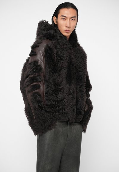 Chaqueta de borrego marrón con una superficie texturizada y esponjosa, y detalles de cuero marrón en las mangas, que presenta detalles fruncidos y un corte holgado.