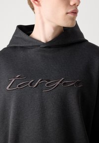 Felpa con cappuccio grigia scura realizzata in tessuto morbido, con un logo ricamato frontale in un filo più scuro. Presenta un cappuccio classico e una vestibilità rilassata.
