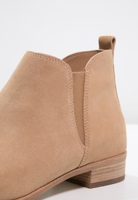 Bottine en daim couleur beige clair avec des panneaux latéraux élastiques, un bout arrondi et un petit talon empilé. Caractérisée par des coutures soignées et une texture lisse.