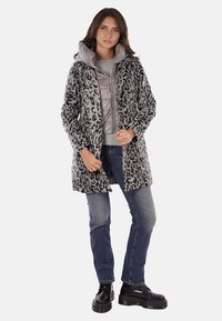 Abrigo de piel de leopardo gris con cierre de cremallera, que lleva debajo una chaqueta acolchada gris. Combinado con jeans azules y botas negras.