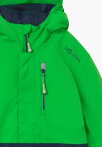 Giacca da esterno impermeabile verde con zip frontale, cappuccio regolabile, due tasche con zip e un accento blu navy all'orlo.