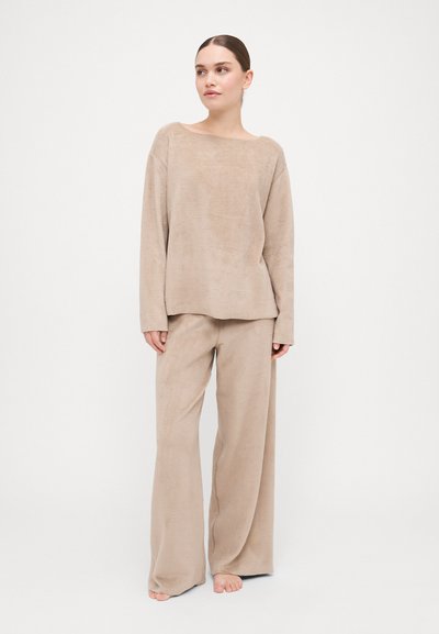 Beige loungewear set made of soft, textured fabric. Long-sleeve top with wide neckline and loose-fitting palazzo pants.
