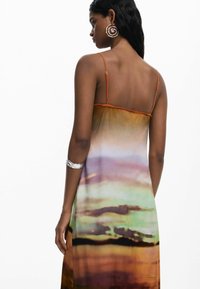 Vista posteriore di un maxi dress multicolore in gradiente con spalline sottili, che presenta tonalità di arancione, verde e viola, con una texture liscia.