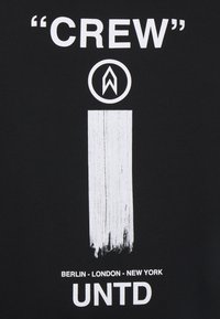 T-shirt nera con testo bianco in grassetto: “CREW,” un logo circolare e un grafiche a pennellate. Città elencate in basso con un carattere moderno.
