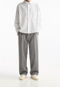 Camisa de botones a rayas en blanco y azul marino, combinada con pantalones de traje grises con pliegues. Incluye un bolsillo en el pecho y zapatillas blancas.