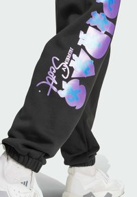 Schwarze Sweatpants mit lila und blauen Grafiken, elastischen Bündchen und dem Schriftzug "JEREMY SCOTT" in einer fließenden Schrift.