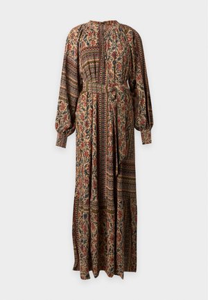 Femme portant une longue robe à fleurs avec de longues manches bouffantes et une ceinture à nouer, debout devant un fond blanc uni.