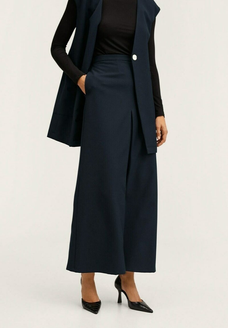 Pantaloni larghi blu navy con vita alta, tessuto texture, tasche laterali, abbinati a un top fitted nero e tacchi a punta neri.