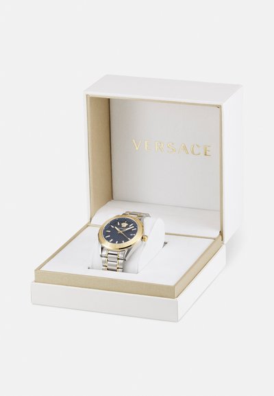 Versace watch in a box, featuring a blue dial, gold-tone bezel, silver stainless steel bracelet, and prominent brand logo.
