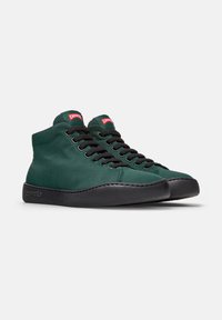 Groene hoge sneakers met zwarte zolen en veters, voorzien van rode "Camp" logo-tags aan de zijkanten. Tegen een effen witte achtergrond.