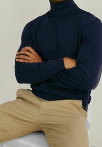 Marinblå polotröja i ribbad stickad design med en figursydd silhuett, kombinerad med beige byxor för en kontrasterande look.