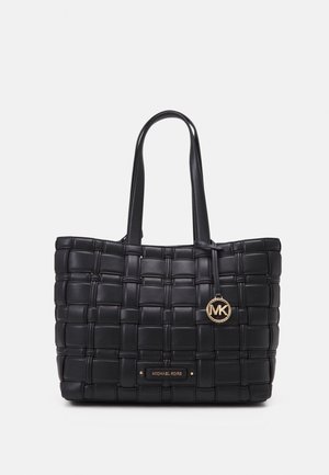 Sort vævet lædertaske med dobbelte håndtag og et gyldent rundt MK-logo vedhæng, med en Michael Kors navneskilt foran.