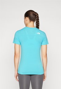 Un t-shirt de sport à manches courtes bleu, en tissu lisse, présente un logo dans le haut du dos. Le t-shirt a une silhouette ajustée et un ourlet incurvé.