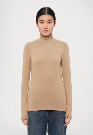 Beige høyhalset genser laget av mykt stoff, med lange ermer og en tettsittende design, kombinert med blå denimjeans.
