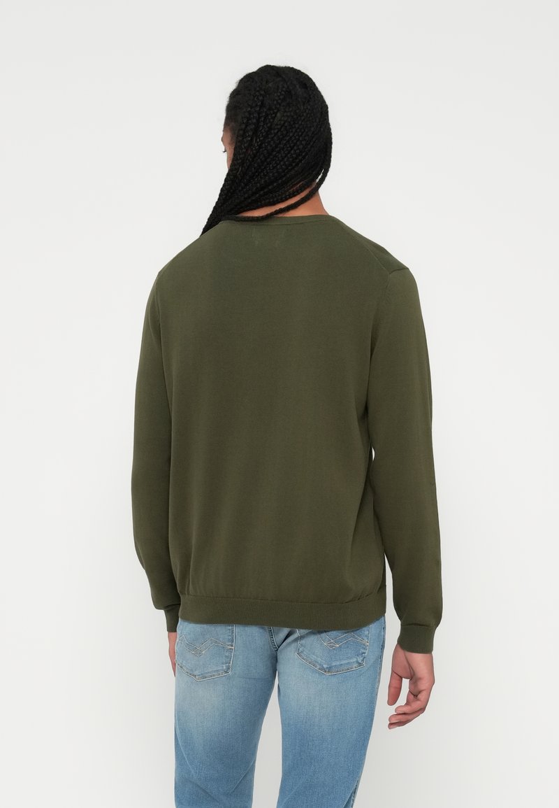 Olivengrüner Pullover mit Rundhalsausschnitt, langen Ärmeln und geripptem Saum. Glatte Textur, normale Passform, kombiniert mit hellblauen Jeans.