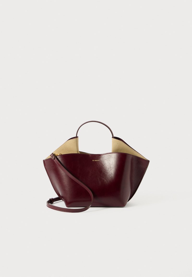 Burgundy läderhandväska med en strukturerad form, som har ett kort handtag, lång axelrem och en kontrasterande beige insida.