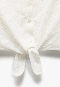 Hvid skjorte med knaplukning i struktureret stof, der har indviklede mønstre, korte ærmer og en bundet detalje ved taljen.