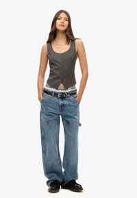 Grijs gestreepte cropped vest met knopen aan de voorkant, gecombineerd met losse blauwe denimbroeken met een brede pijp en zichtbare stikseldetails.