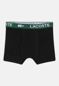 Melni bokserveida apakšbikses, kas izgatavotas no kokvilnas, ar zaļu elastīgu jostas vietu, uz kuras ir balta "LACOSTE" apzīmējuma un krokodila logo.