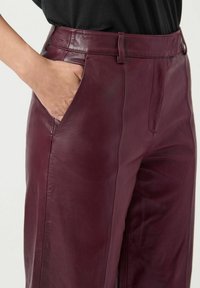 Bordeaux leren broek met een gladde textuur, hoge taille, zijzakken en schone naden. De riemlussen zijn zichtbaar langs de tailleband.