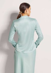 Lichtblauwe satijnen blouse met lange mouwen, een getailleerde pasvorm en een gladde textuur. Opvallende details zijn een subtiele glans en een gebogen zoom.