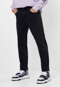 Svarta denimjeans med rak passform, femfickorsdesign och subtil textur. I kombination med klumpiga vita och lila sneakers.