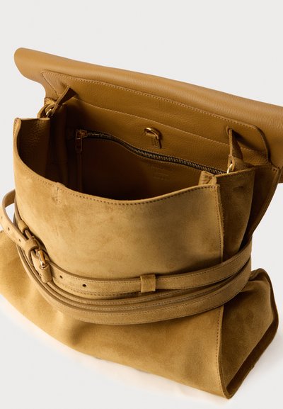 Sac à bandoulière en daim et cuir beige avec rabat pliant, sangle réglable et poche intérieure zippée.