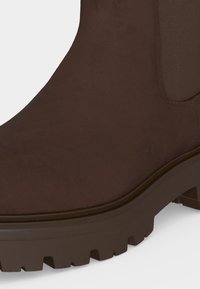 Bottine Chelsea en daim marron avec panneau latéral élastique et semelle crantée épaisse.