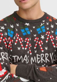 Brun jultröja med röda och blå godisrör, julklappar och snöflingor. Stickad textur med ribbat halsringning och ärmslut.