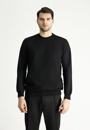 Schwarzer Rundhalsausschnitt-Hoodie aus glattem Stoff mit langen Ärmeln und gerippten Bündchen, kombiniert mit schwarzen, taillierten Hosen.