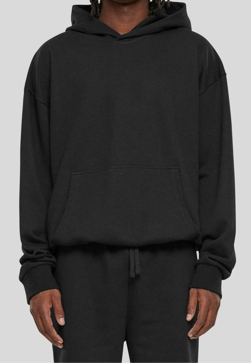 Felpa nera oversize realizzata in tessuto morbido, con tasca frontale, cappuccio con coulisse e polsini a coste, abbinata a pantaloni coordinati.