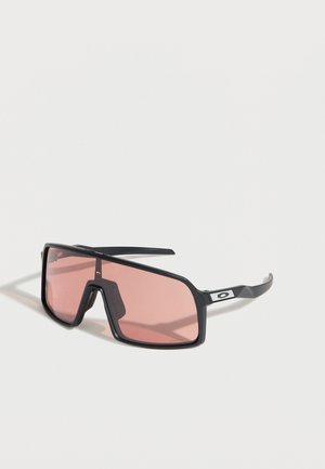 Rechthoekige zonnebril met zwart montuur en roze getinte glazen die op een wit oppervlak met schaduw ligt.