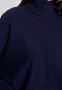 Merinotakke navy, valmistettu neulotusta kankaasta, jossa on röyhelötekstuuri ja tiukka muotoilu. Pehmeä ja kevyt materiaali.