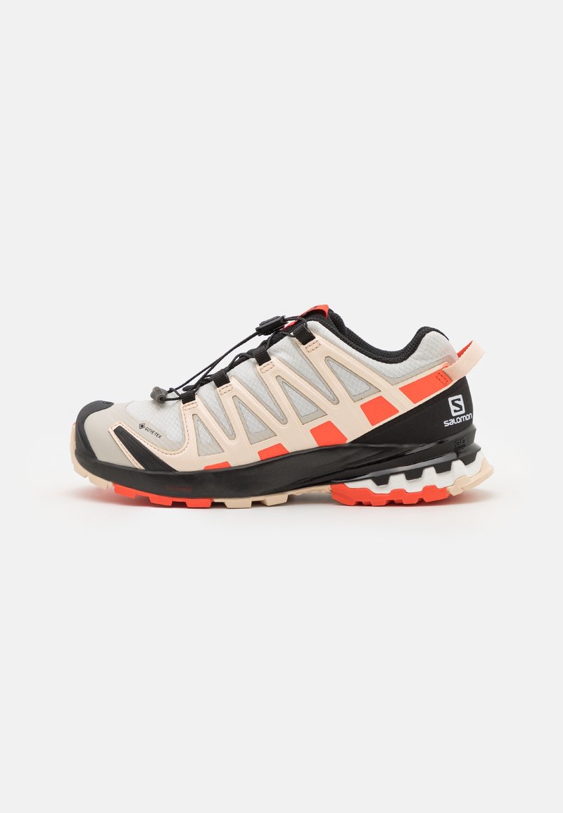 Chaussure de trail running gris clair et orange avec semelle noire, matériau Gore-Tex, système de laçage rapide et logo de la marque sur le talon.