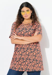Top de estampado floral en gris con vibrantes flores coral. Mangas cortas y escote en forma de V con diseño entrelazado. Combinado con jeans azules.