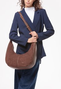 Borsa hobo marrone con esterno in suede e pelle strutturata, forma curva e tracolla regolabile marrone. Dettaglio del logo dorato nell'angolo inferiore.