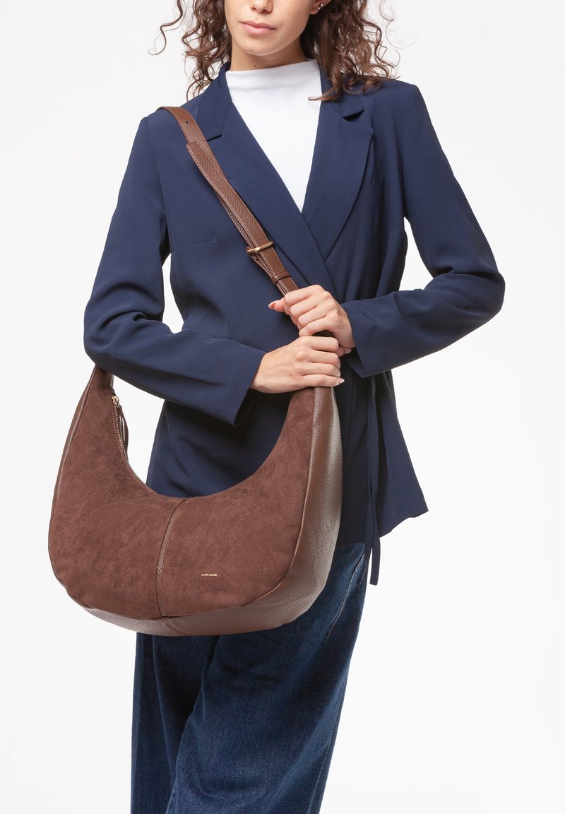 Borsa hobo marrone con esterno in suede e pelle strutturata, forma curva e tracolla regolabile marrone. Dettaglio del logo dorato nell'angolo inferiore.
