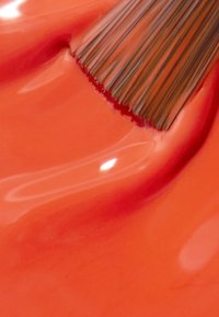 Klart orange nagellack med en glansig yta, med en pensel med fina borst som vilar på den släta ytan och skapar en liten våg.