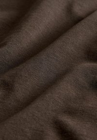 Brūns audums ar smalku tekstūru, kas rāda mīkstas krokas un gludu virsmu. Materiāls izskatās viegls un elpojošs.