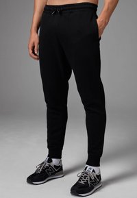 Pantalones joggers negros con cintura elástica y cordón. Presentan bolsillos laterales y perneras ajustadas, fabricados con tejido suave y elástico.