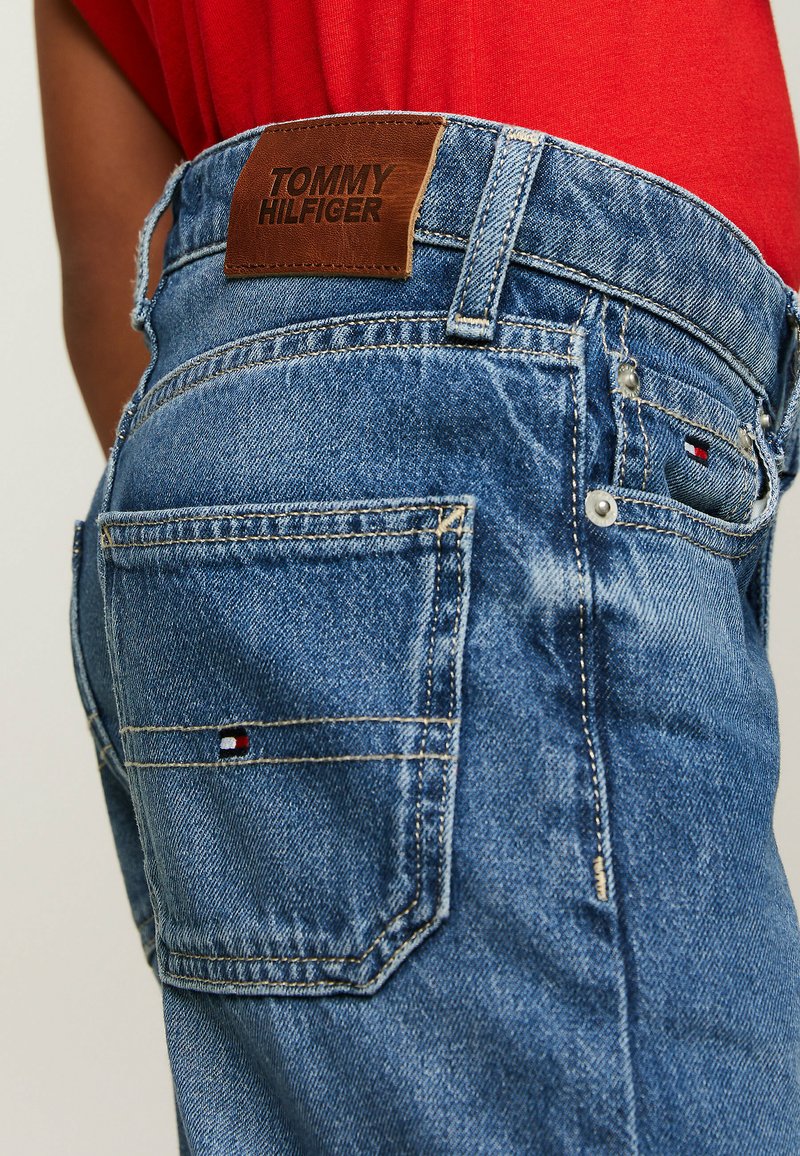 Jeans in denim di colore azzurro chiaro con un'etichetta in pelle Tommy Hilfiger sulla vita, cuciture visibili e dettagli del logo sulle tasche posteriori.