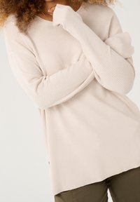 Hellbeiger gerippter Pullover aus strukturiertem Stoff, mit langen Ärmeln und weiter Passform, einem abgerundeten Ausschnitt und Seitenschlitzen.